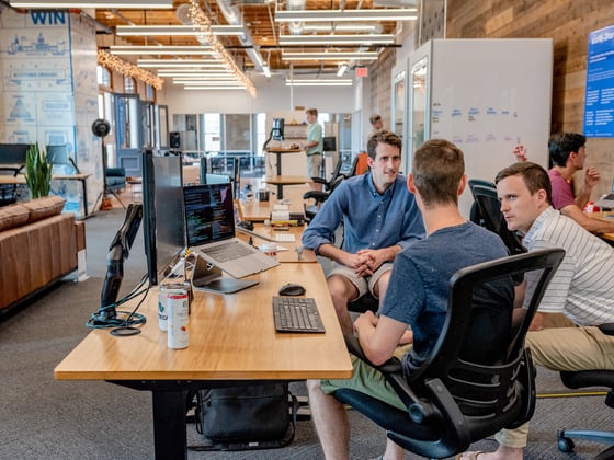 Three men around a computer in a coworking space